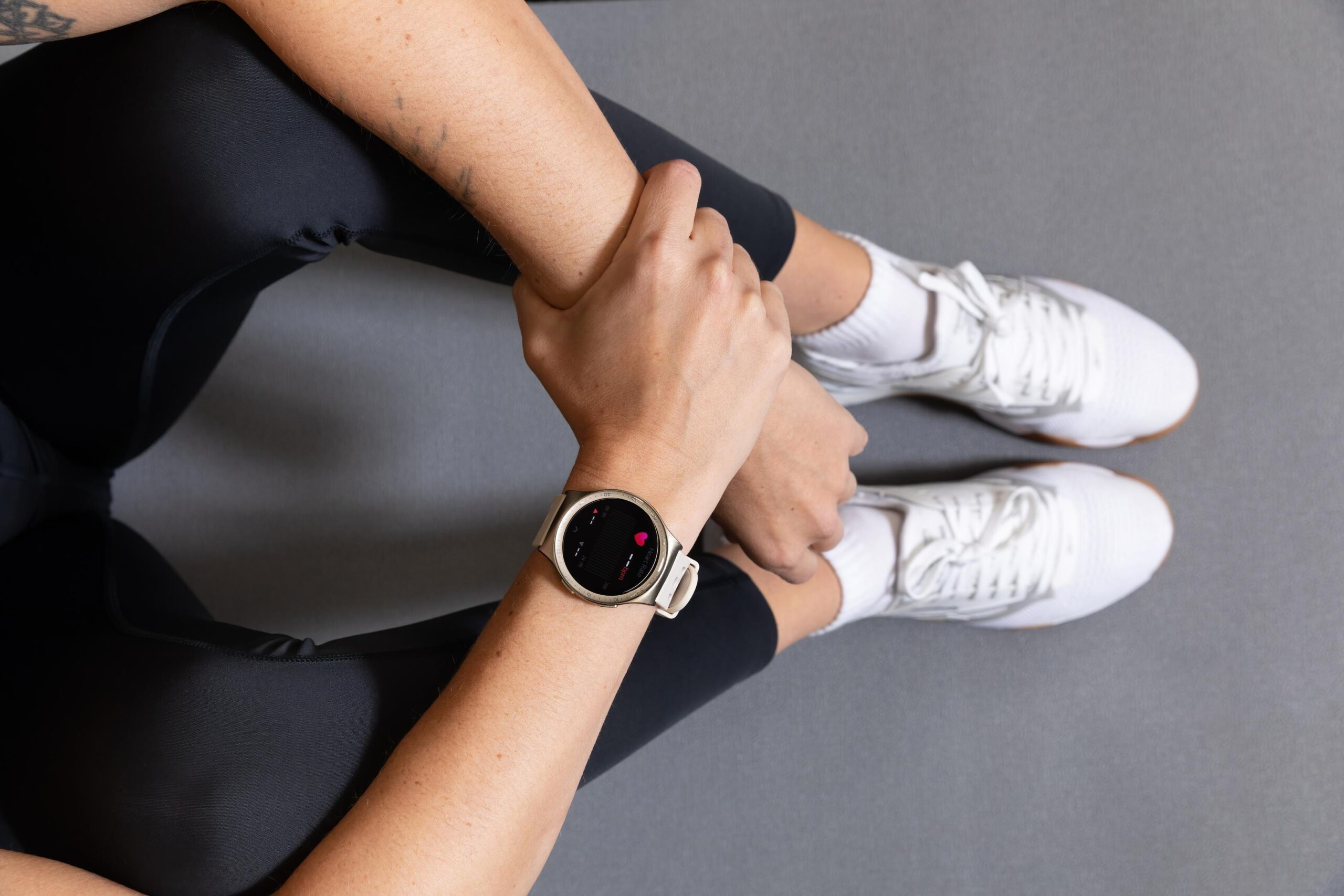 A person wearing a smartwatch while seated in workout clothing, using the device to monitor heart rate and fitness data during exercise or recovery. The smartwatch highlights health tracking features commonly used for wellness, activity monitoring, and workout support.