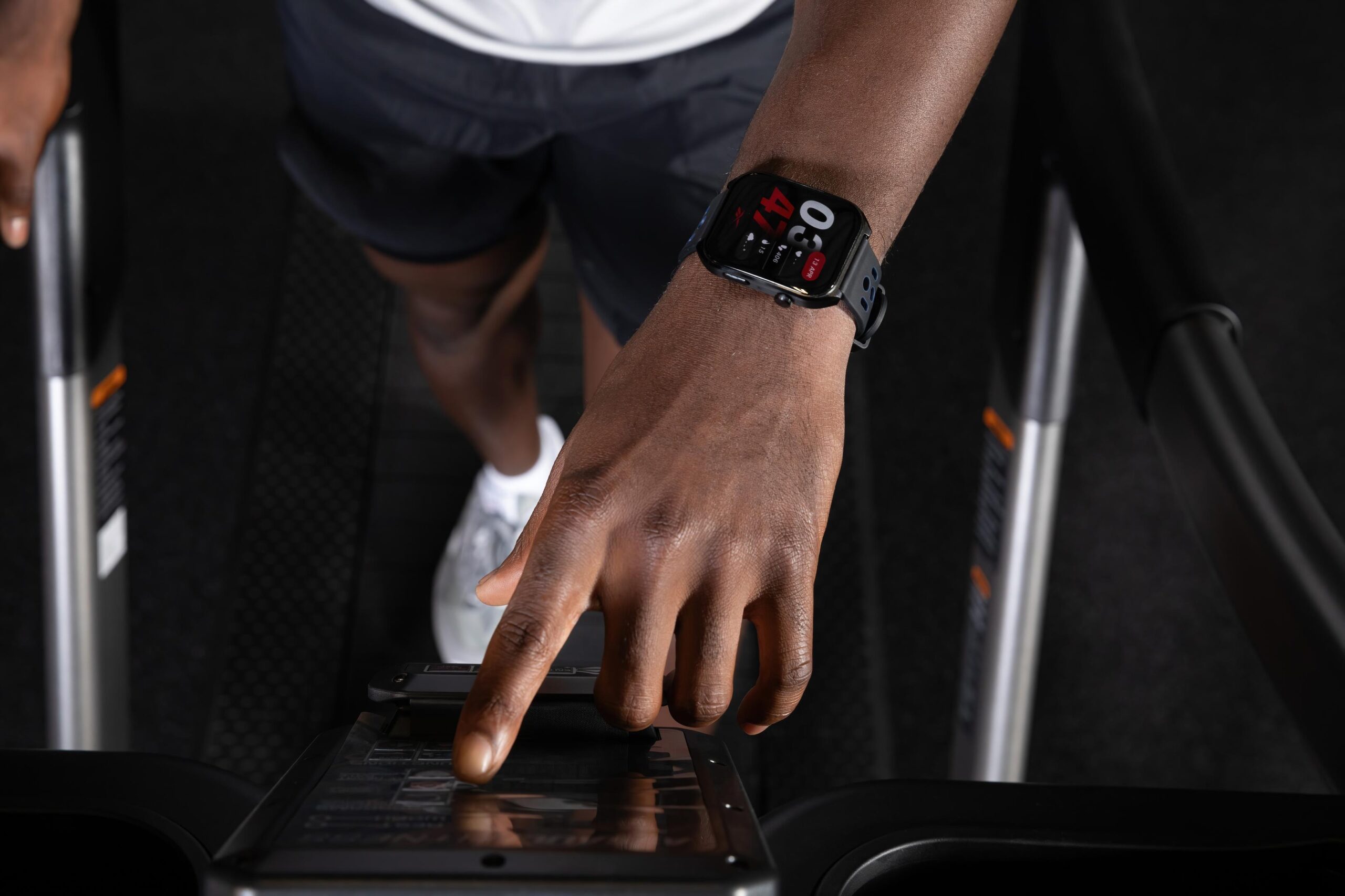 “Person using a Reebok smartwatch while adjusting treadmill settings at the gym.”